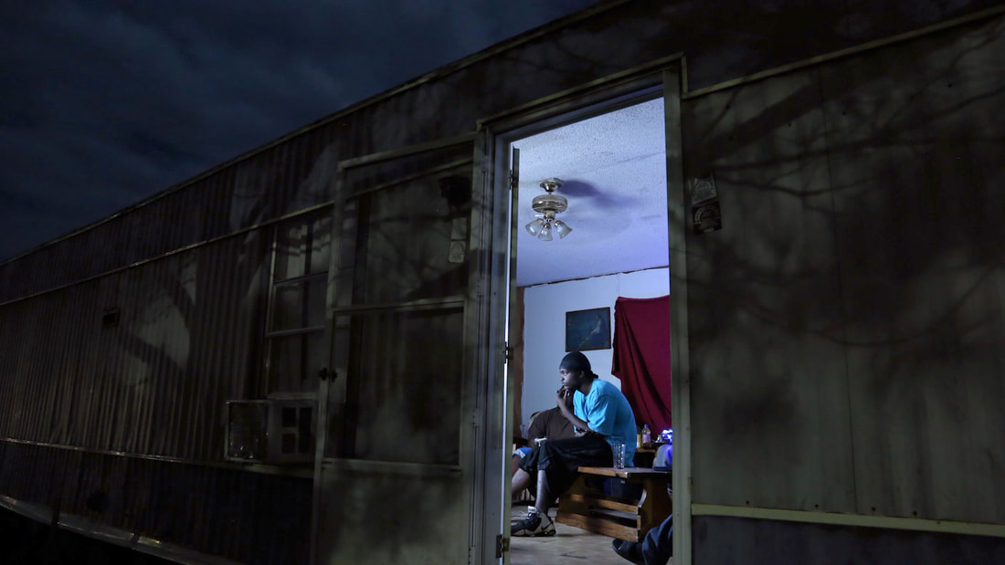Hale County This Morning, This Evening — a young man inside a trailer home at night, seen through the open door
